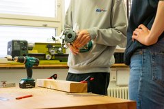Zwei junge Menschen stehen vor einer Arbeitsplatte, auf der Werkzeuge stehen