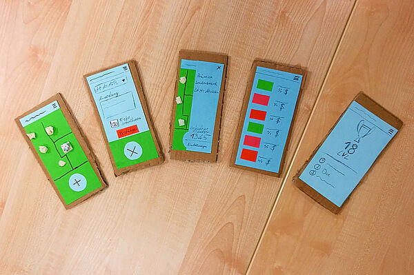 Fünf aus Karton gebastelte Handys mit unterschiedlichen Bildschirmen