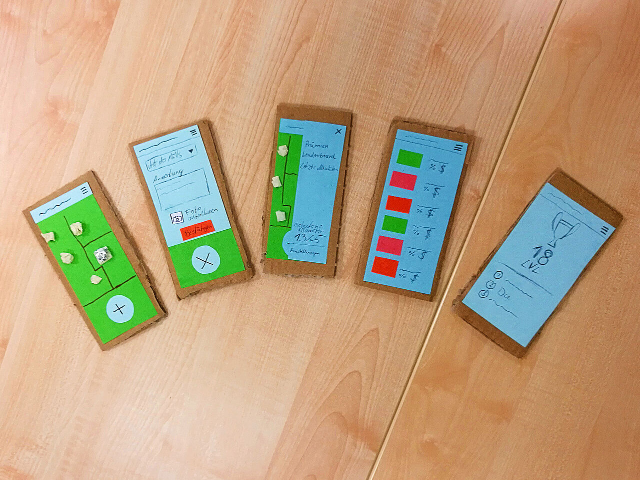 Fünf aus Karton gebastelte Handys mit unterschiedlichen Bildschirmen.